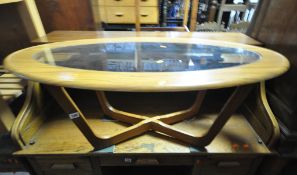 A TEAK EFFECT OVAL COFFEE TABLE, with a glass insert, raised on cross shaped legs, width 107cm x