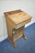 A PINE LECTERN, with two ink well slots, a pen section, a hinged lid, and a single door, width