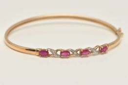 A 9CT GOLD RUBY AND DIAMOND BANGLE, set with four oval cut rubies, interspaced with single cut