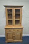 AN EARLY 20TH CENTURY PINE BOOKCASE, with double glazed doors, atop a base with two drawers and