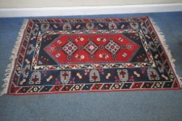A RED AND BLUE GROUND RECTANGULAR WOOLLEN RUG, with repeating geometric patterns, surrounded by a