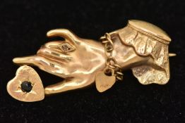 A 9CT GOLD BROOCH, in the form of a ladies hand with bracelet, embellished ring holding a sapphire