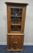 A MODERN PINE CORNER CUPBOARD, fitted with a single lead glazed door, over double cupboard doors,