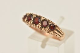 A YELLOW METAL GEM SET RING, five circular cut garnets prong set in yellow metal with scrolling
