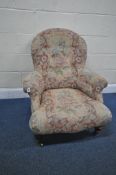 A LOW PUTTON BACK ARMCHAIR, with foliate upholstery, raised on turned front legs, with brass