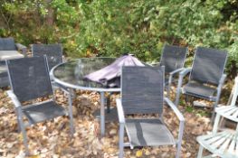 A GREY PAINTED STEEL FRAMED AND SMOKED GLASS GARDEN TABLE with six matching chairs, parasol and