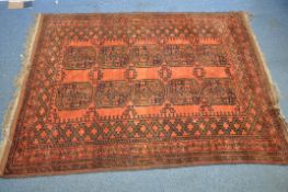 A RED GROUND AFGHAN WOOLLEN RUG, with ten central medallions, surrounded by a multi-strap border,