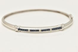 A WHITE METAL GEM SET HINGED BANGLE, set with a row of square cut blue sapphires and three small