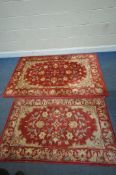 TWO RED GROUND WOOLLEN RUGS, with repeating foliate patterns, surrounded by a border, largest rug