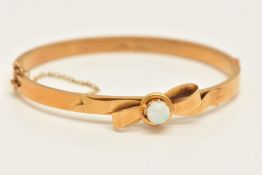 A 15CT GOLD OPAL HINGED BANGLE, a yellow gold hollow bangle with bow detail and a centrally set