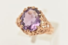 A 9CT GOLD AMETHSYT DRESS RING, set with an oval cut amethyst claw set to the open work textured