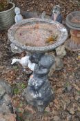 A CONCRETE BIRDBATH, in the form of a small child seat on rocks holding aloft a ewer, and bowl on