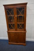 A REPRODUCTION YEW WOOD BOOKCASE, the double glass doors enclosing two shelves, atop a base with a