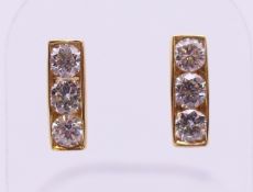 A pair of 18 ct gold three stone diamond earrings. 1.25 cm high.