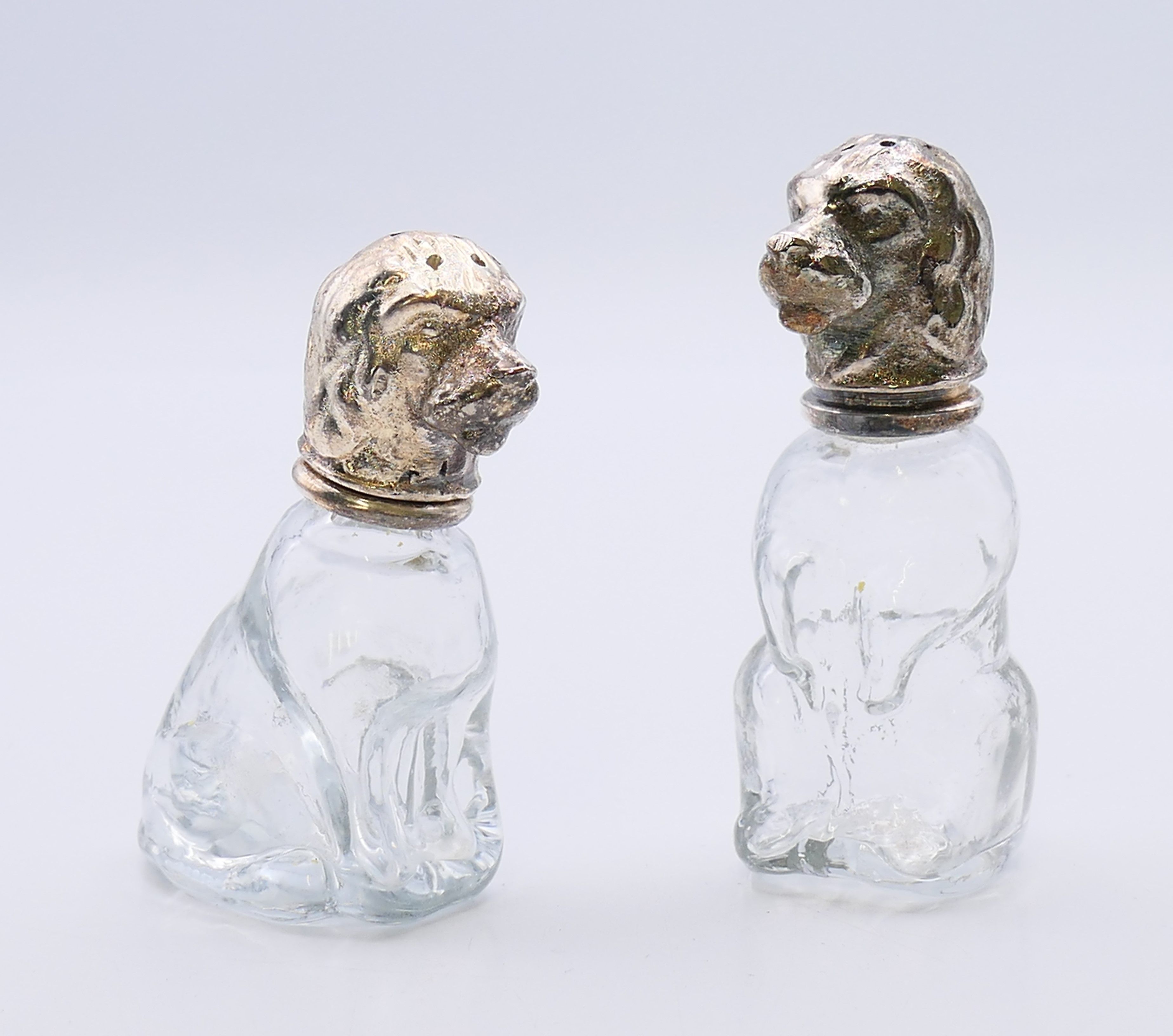 A pair of glass and white metal peppers formed as dogs. 8 cm and 7 cm high respectively.