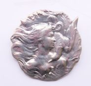 A silver Art Nouveau style female with flowing hair and a dove brooch. 3.75 cm diameter.
