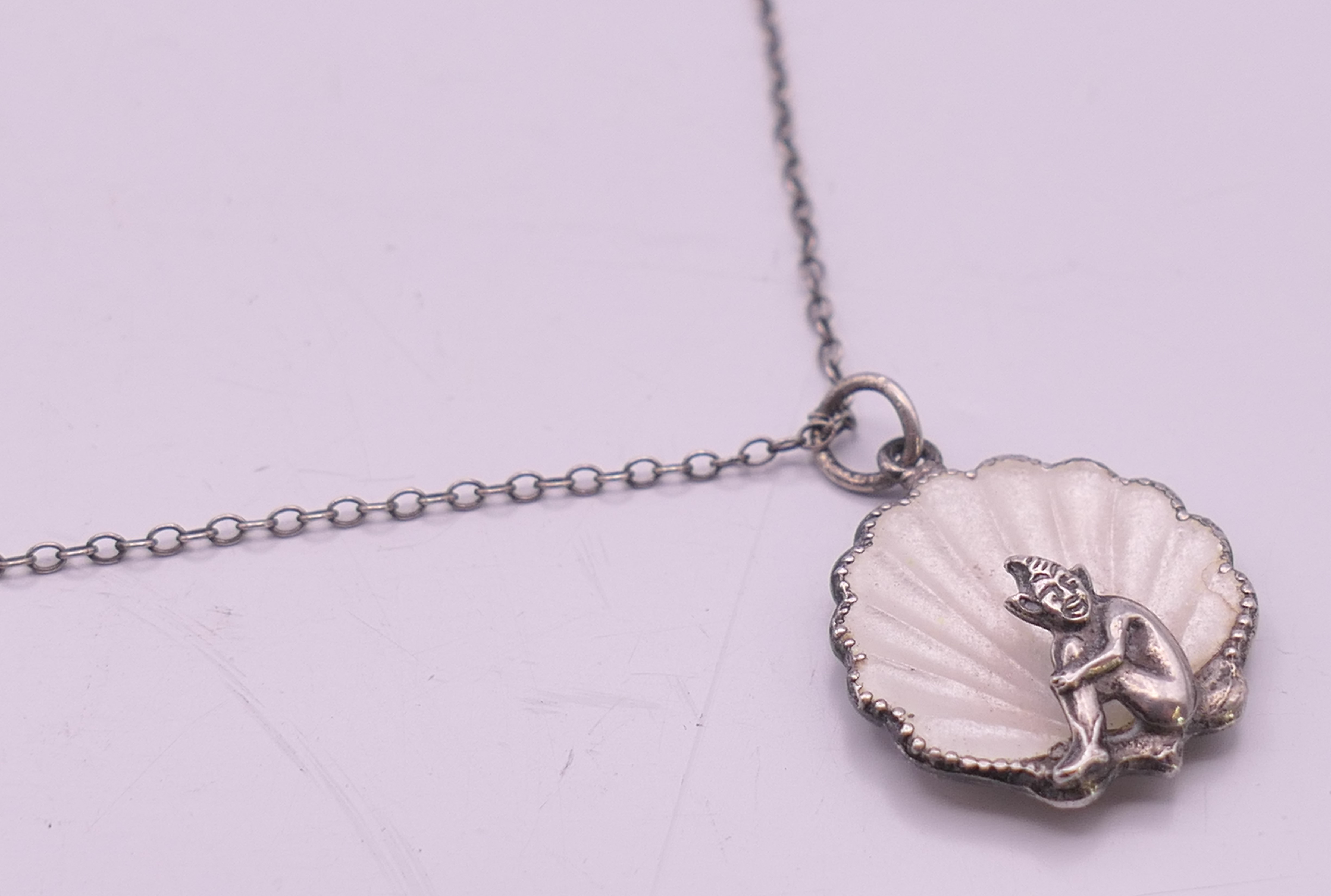A silver and enamel pixie in a shell pendant on a silver chain. Pendant 2 cm high, chain 46 cm long. - Image 3 of 6