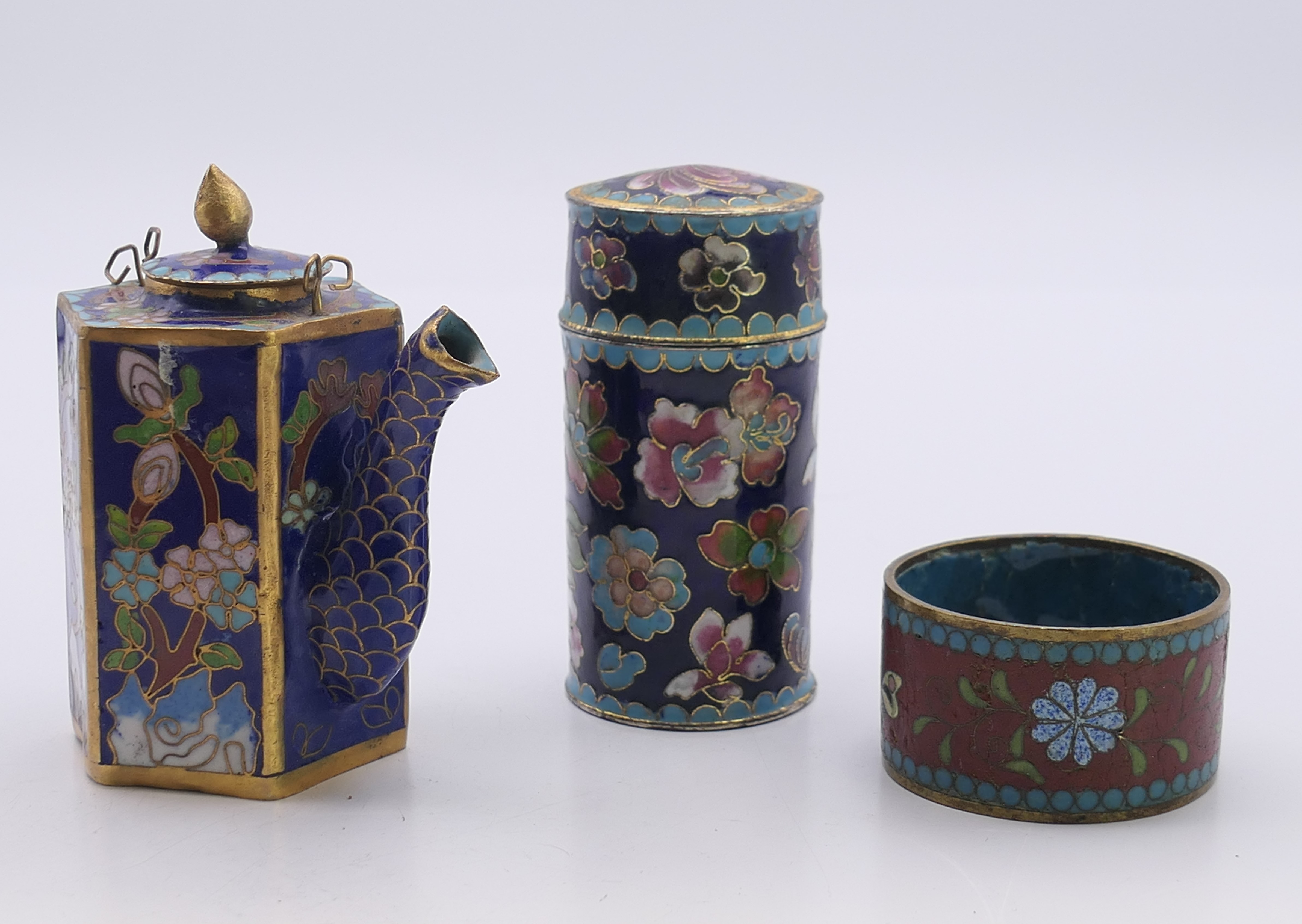 Three small Chinese cloisonne items comprising a miniature teapot, a lidded jar and a napkin ring.