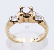A 9 ct gold diamond solitaire with trapeze cut diamond shoulders. 3.8 grammes. Ring size L.