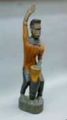 A carved wooden figure playing an African drum. 95 cm high.