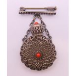A glass scent bottle in a white metal filigree casing set with coral and mounted on a chain and
