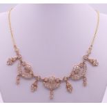 An unmarked high carat gold and diamond 'swags and tails' necklace on an unmarked 22 ct gold chain.