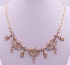An unmarked high carat gold and diamond 'swags and tails' necklace on an unmarked 22 ct gold chain.