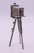 An unmarked white metal model of a tripod bellows camera. 12 cm high.