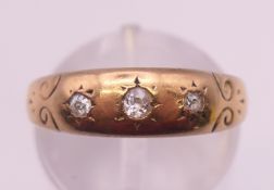An unmarked gold three-stone diamond gypsy ring. Ring size M/N. 3.7 grammes total weight.