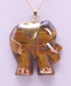 A carved tiger's eye and 14 K gold pendant in the form of an elephant on a 9 ct gold chain.