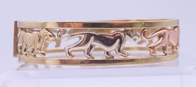 A 9 ct tri-colour gold bangle bracelet with openwork panther decoration. 1.