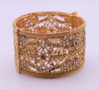 An Indian yellow metal bangle set with coloured stones and pearls.