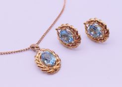 A 9 ct gold pendant on chain and a matching pair of earrings, each set with a blue stone.