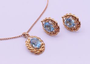 A 9 ct gold pendant on chain and a matching pair of earrings, each set with a blue stone.