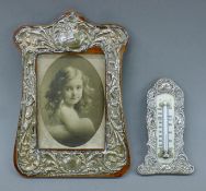 An Art Nouveau silver photograph frame and a silver-framed thermometer. The former 23 cm high.