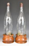 Two bar top, engraved wine bottles with taps raised on turned wooden stands, H59cm