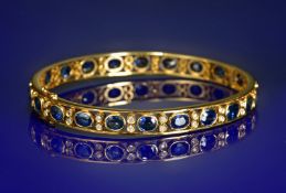 An 14k gold bangle set with twenty two oval cut sapphires each approximately 0.3ct, and forty four