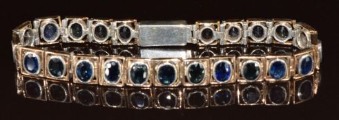 A white metal bracelet set with twenty three oval cut sapphires, testing as 9k white gold, the