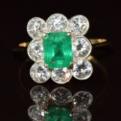 An 18k gold ring set with an emerald cut emerald of approximately 1ct surrounded by eight round