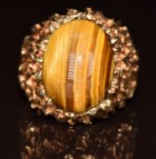 A 1970s 9ct gold ring set with a tiger's eye cabochon, with textured pierced shoulders, 8.7g, size