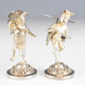Two Eastern silver figurines comprising a lady wearing a hat and carrying two baskets on a pole, the