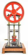 Inverted single cylinder live steam engine with turned column supports, driving a spoked flywheel,
