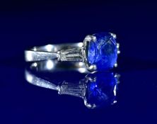 A platinum ring set with a cushion cut sapphire of approximately 3.1ct flanked by two tapered