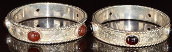 A pair of matched silver bangles with textured finish, one set with agate cabochons the other with