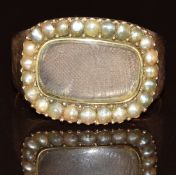 A 9ct rose gold mourning ring set with a locket compartment surrounded by seed pearls, the ring