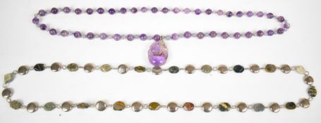 A large beaded amethyst necklace with a carved pendant depicting fruit and a bird, and a white metal