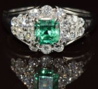 A platinum ring set with an emerald cut emerald of approximately 0.7ct surrounded by round cut