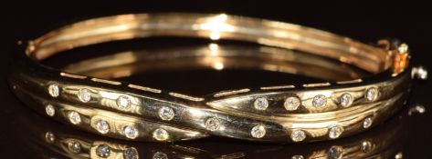 A 9ct gold bangle set with round cut diamonds in a cross over design, the total diamond weight