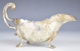 George VI hallmarked silver sauce boat with scroll handle, raised on three hoof feet, Sheffield