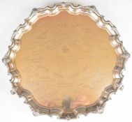 George V hallmarked silver salver with shaped edge and raised on three scroll feet, with inscription